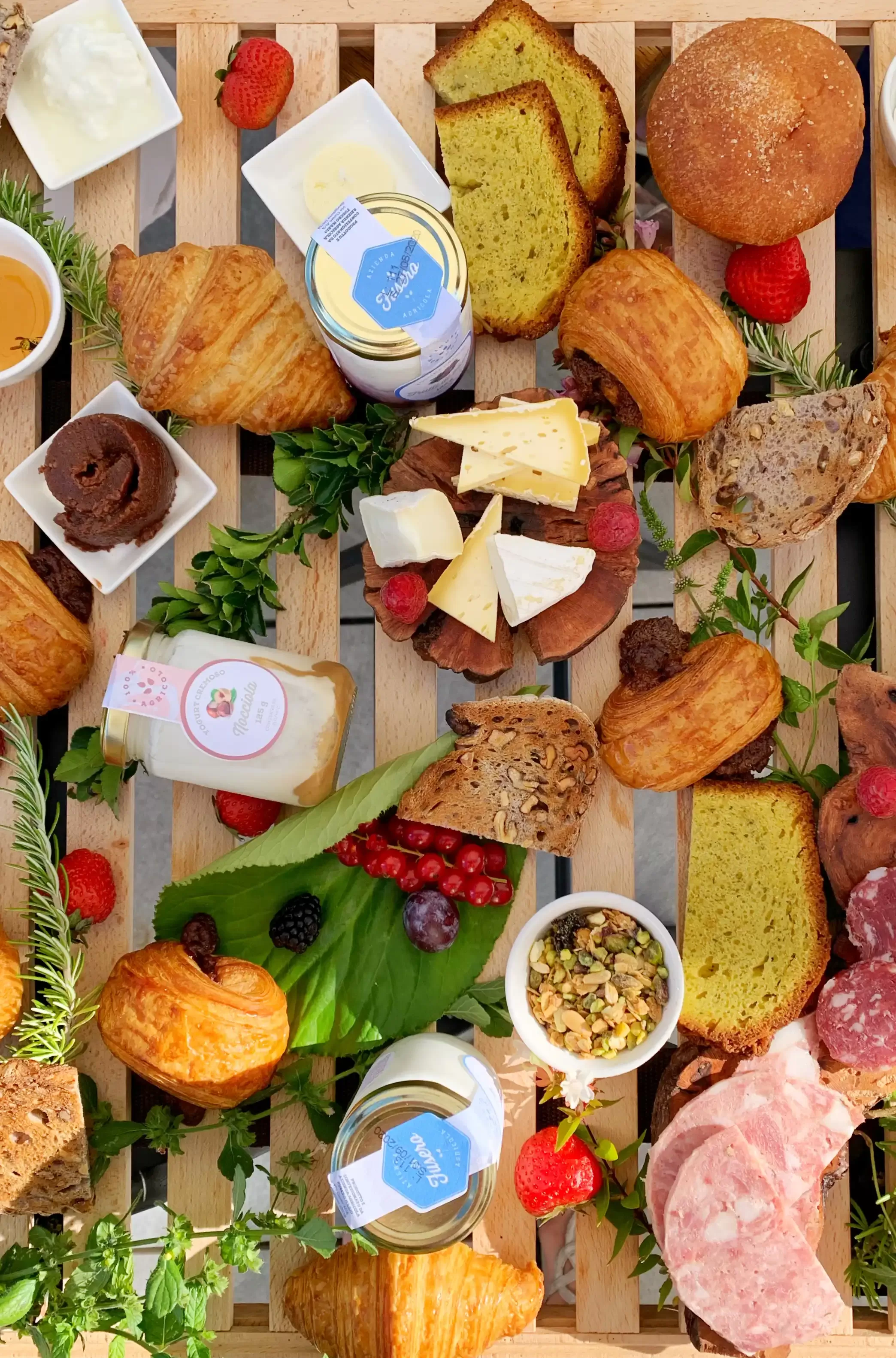 Freshly baked croissants and cakes, yoghurt, cheeses, cold cuts, nuts, berries, and honey arranged on a massive wooden board at Réva Resort breakfast.