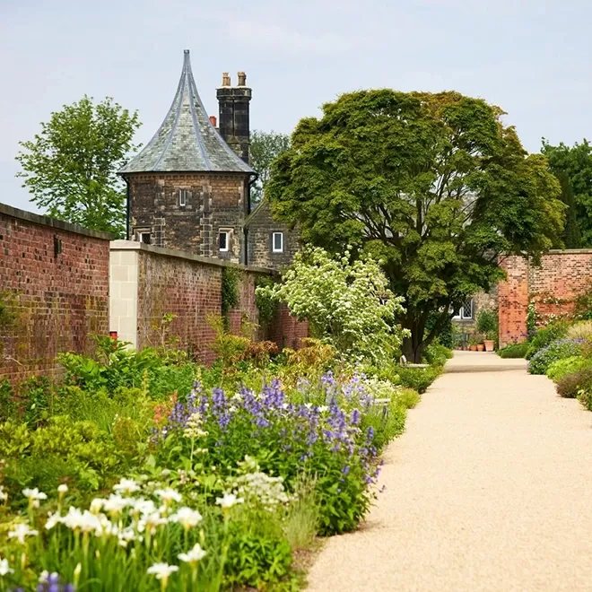 Pathway surrounded by old brick walls and buildings and beautiful flower-filled gardens in RHS Garden Wisley, Woking
