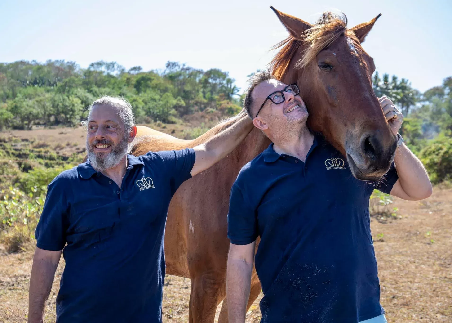 Men stroking and hugging horse in nature at Reach & Conquer Sumba, Indonesia