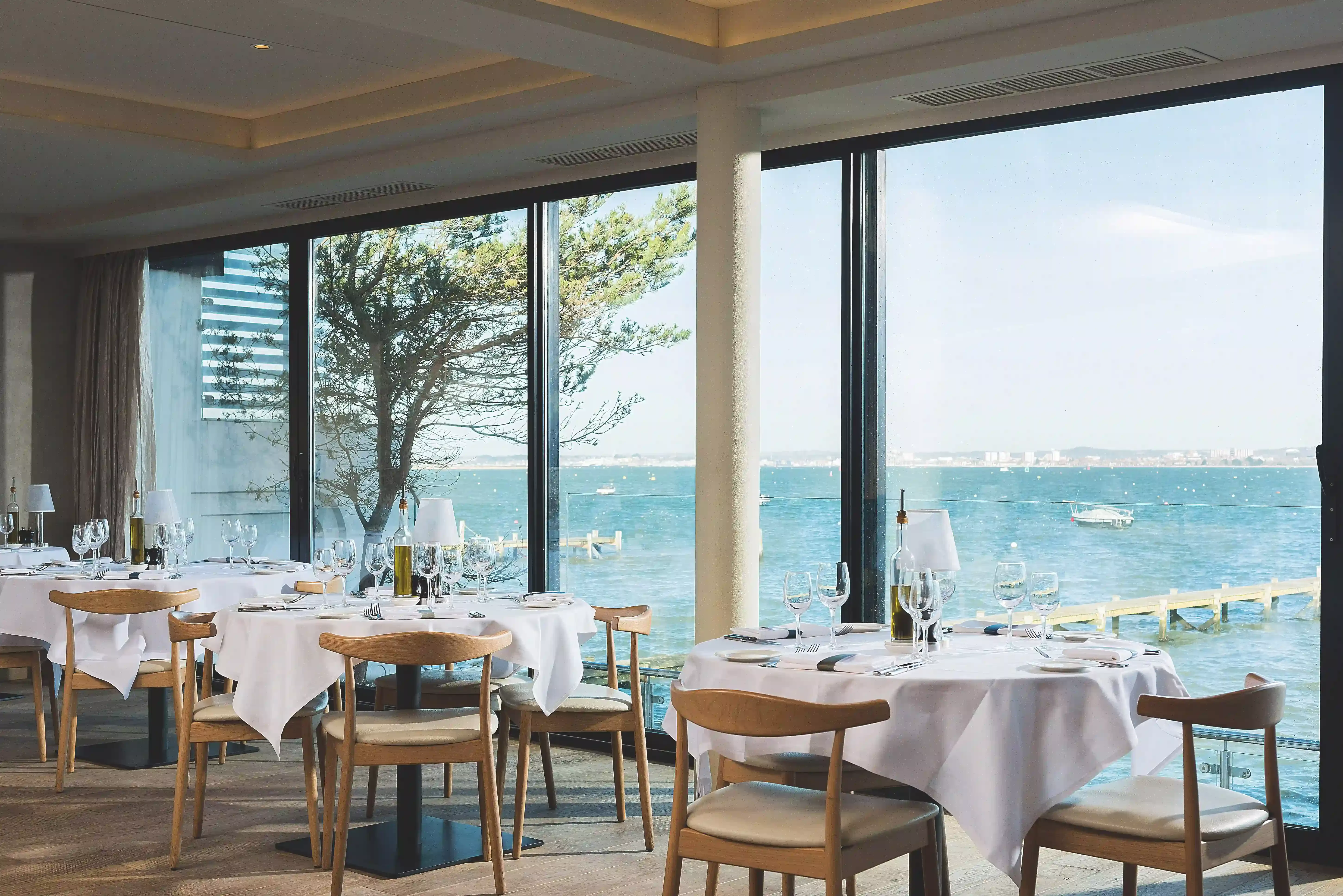 Inside interior of set round dining tables and chairs inside restaurant Rick Stein Sandbanks overlooking view of the sea.