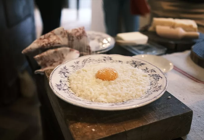 A blue and white patterned plate with white rice topped with a raw egg yolk sits on a wooden surface, with a napkin and blocks of butter in the background.