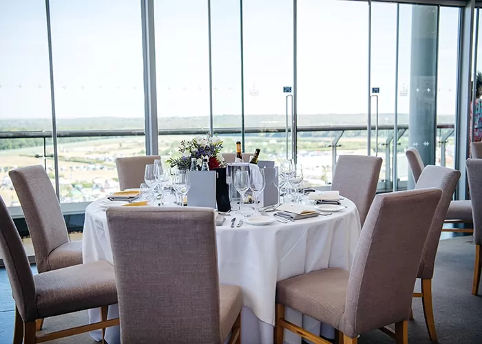 Ascot Royal Enclosure’s round table and chairs with fine dining set up by a glass window and view of the racecourse at the Panoramic Restaurant