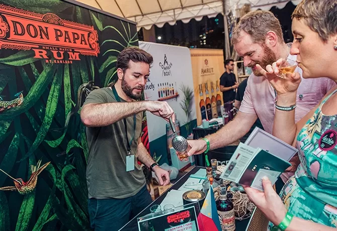 Man on cocktail stand pouring drinks for guests at the Singapore Cocktail Festival