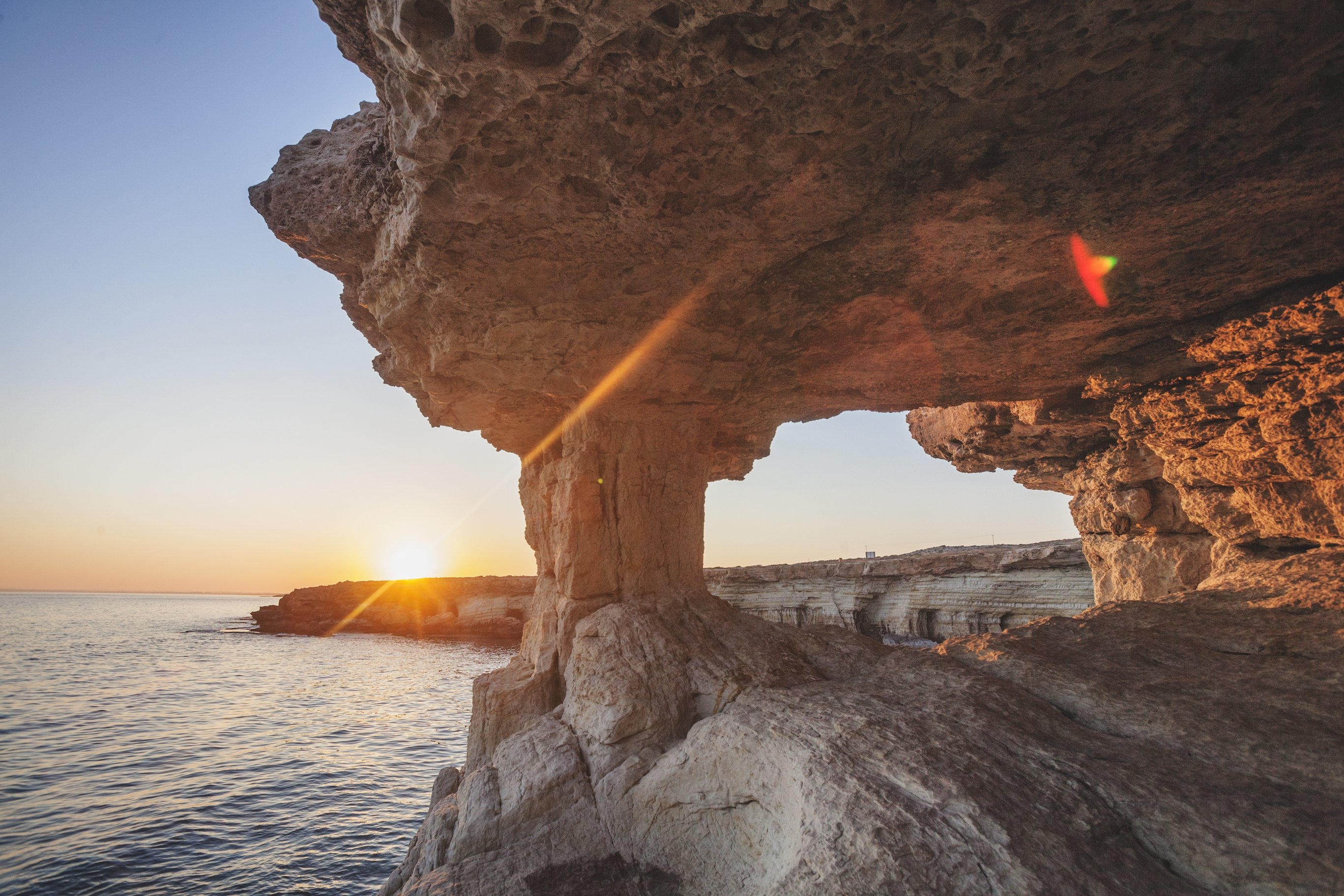 View from inside natural eroded stone sea caves with natural holes giving a view of the sunset over the sea and caves.