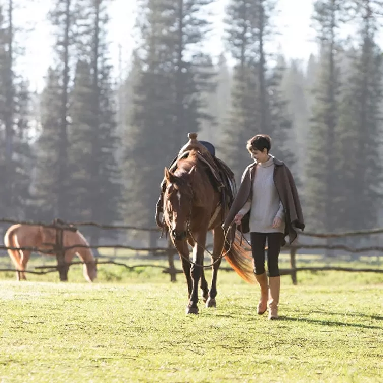 Women smiling walking horse through paddock in the sun at Sensei Lanai, A Four Seasons Resort, Hawaii