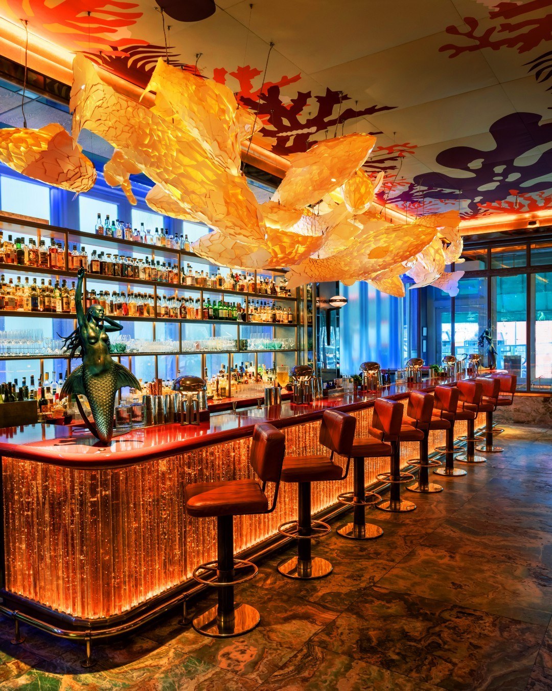 Luxurious colourful long bar and row of bar stools with fish sculptures and lit up shelves of alcohol at Sexy Fish