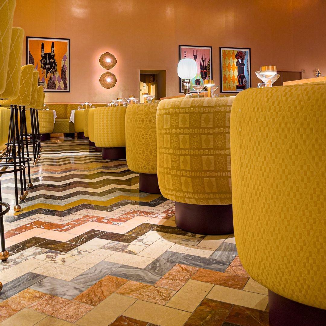 Colourful zig zag designed floor below row of yellow abstract printed rounded chairs in Sketch restaurant