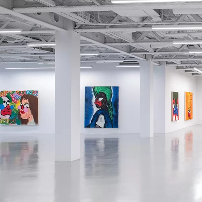 A bright, modern art gallery with white walls and polished floors displays several colorful paintings featuring abstract faces with exaggerated red lips and expressive features.