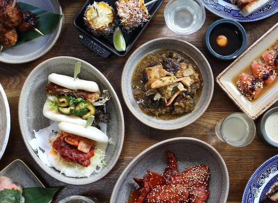 Small plates displaying food, bao buns, meats, skewers and more in rounded plates at Savour.