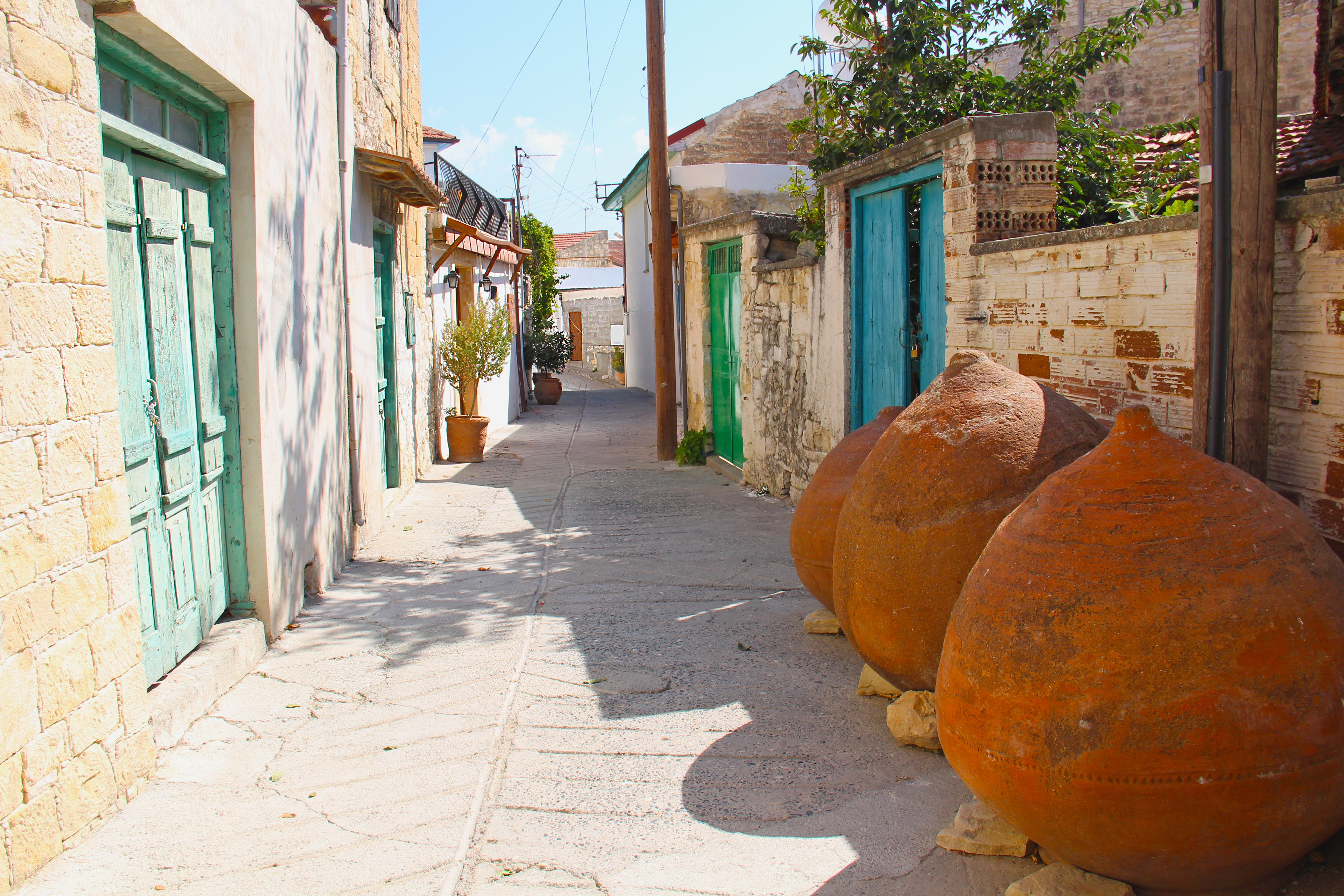 Street in Omodos with blue and green doors, brick walls and orange ball sculptures.