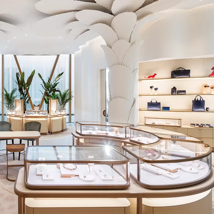 A luxurious jewelry store interior with elegant display cases, designer handbags on shelves, large indoor plants, soft lighting, and sculpted architectural details resembling large white leaves.