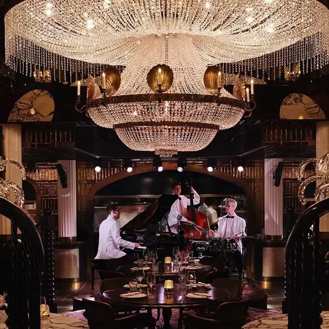 Band in Tuxedo's playing underneath grand chandelier and luxury restaurant The Maine, Mayfair, London