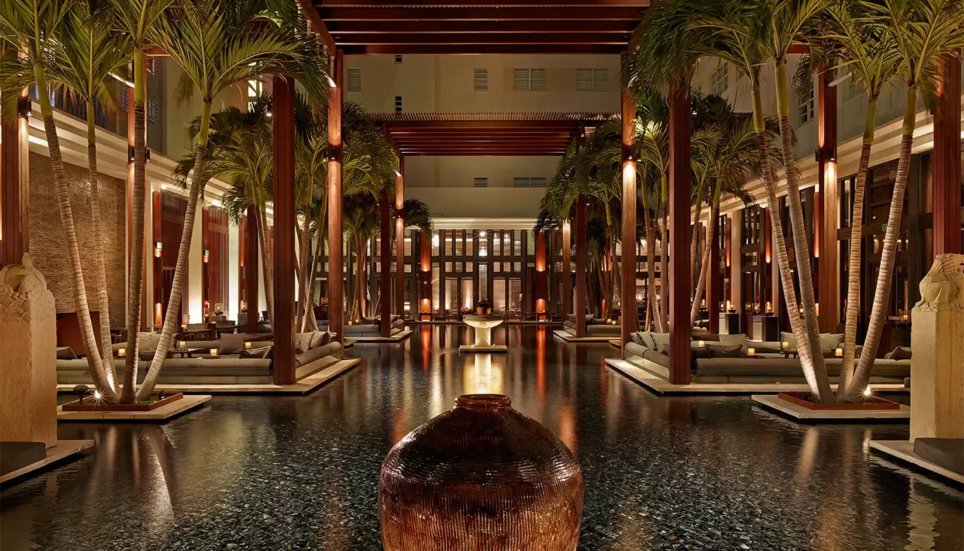 Grand indoor pool surrounded by palm trees and mood lighting