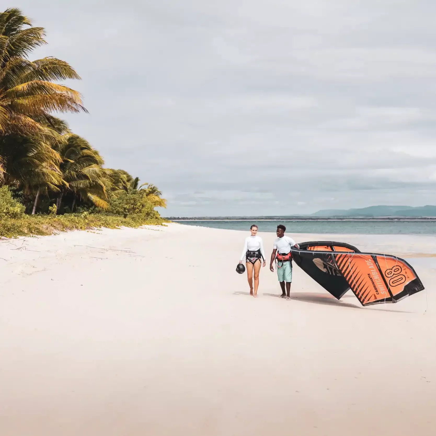 Man and women walking along beach with kiteboard at Time Tide Miavana Madagascar