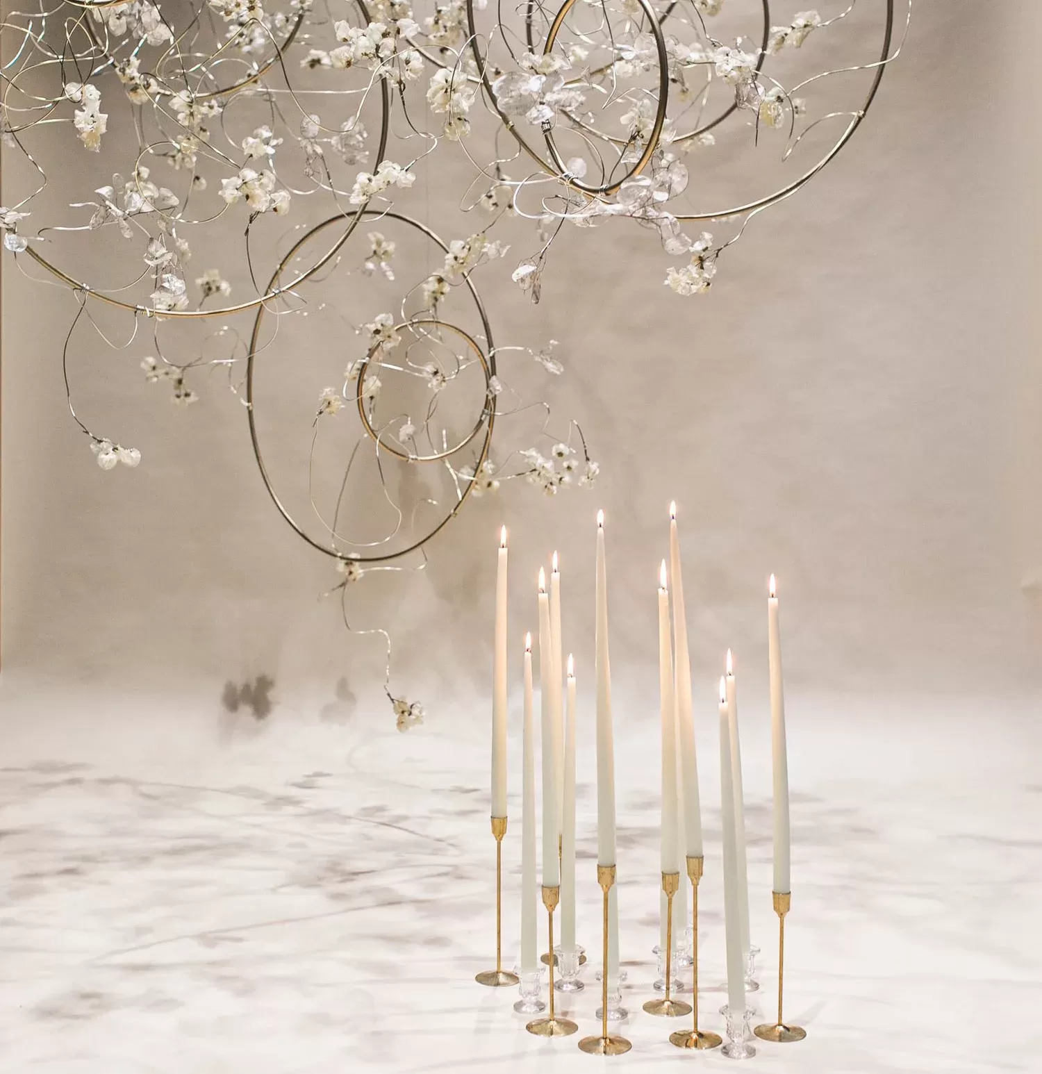 Arrangement of white candles on gold candle stick holders in a white themed room with white flowers.