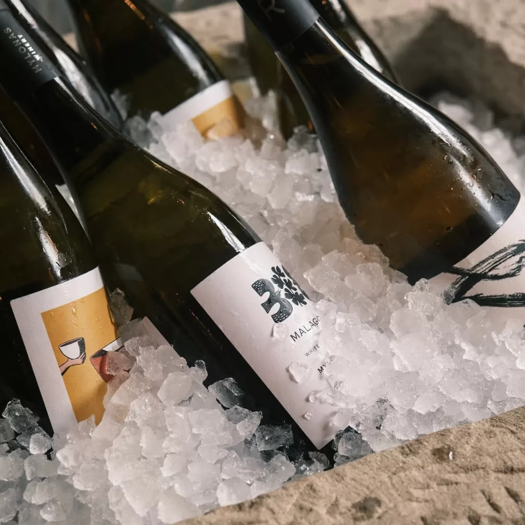 Several wine bottles are arranged in a bed of crushed ice, with condensation on the glass. The bottles have different labels and are lying at various angles, suggesting they are being kept chilled for serving.