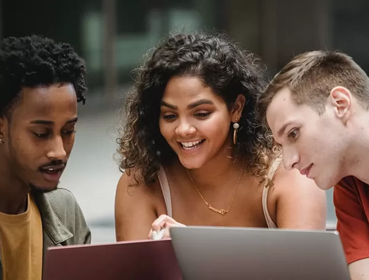 Three young adults smiling and looking at computer screens