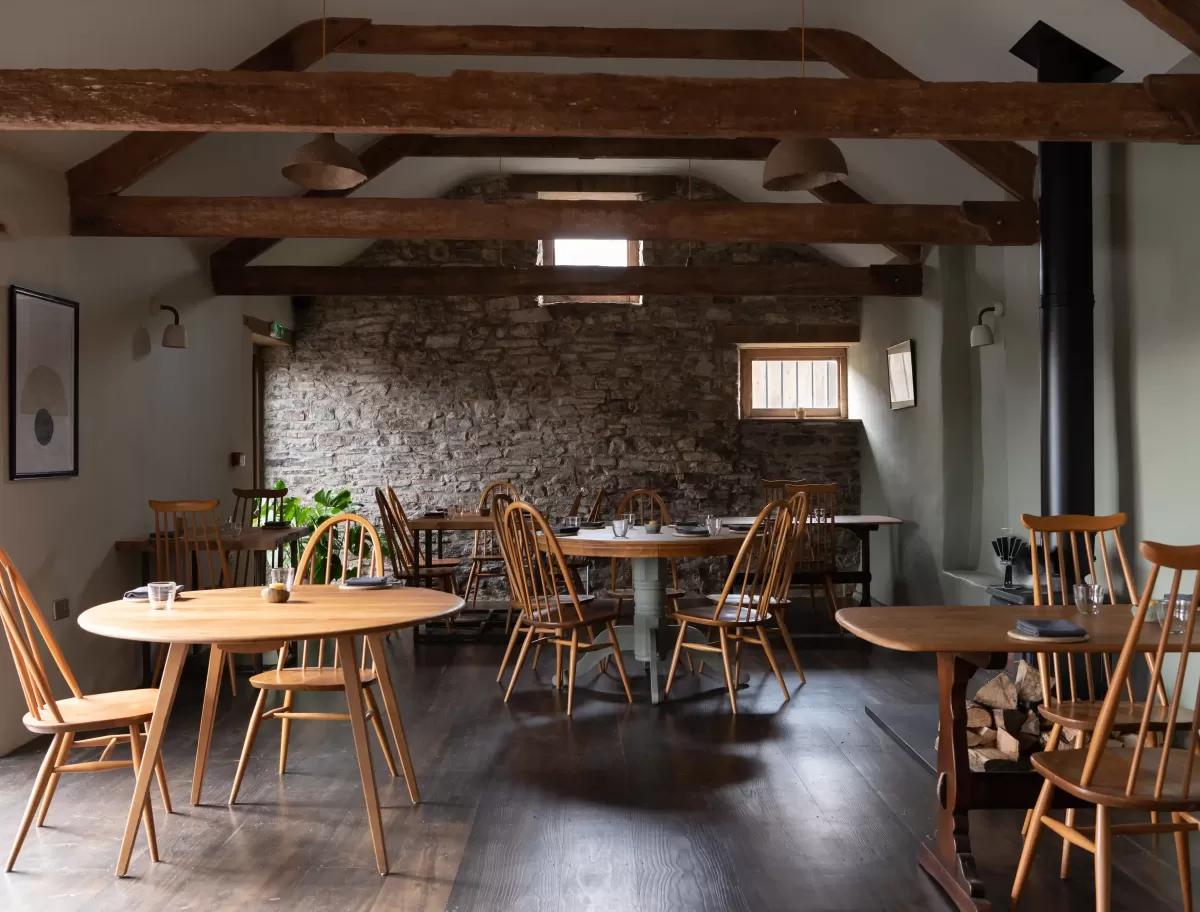Quint cottage style restaurant interior with Cornish stone walls and round wooden tables under wooden beamed roof at Crocadon Farm, Cornwall