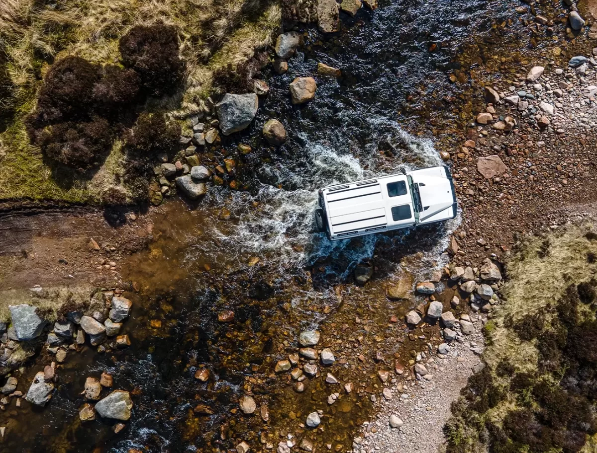 Birdeye eye view of the INEOS Grenadier by Sir Jim’s lieutenants off-road driving through water and rocks in the Cairngorms, Scotland.