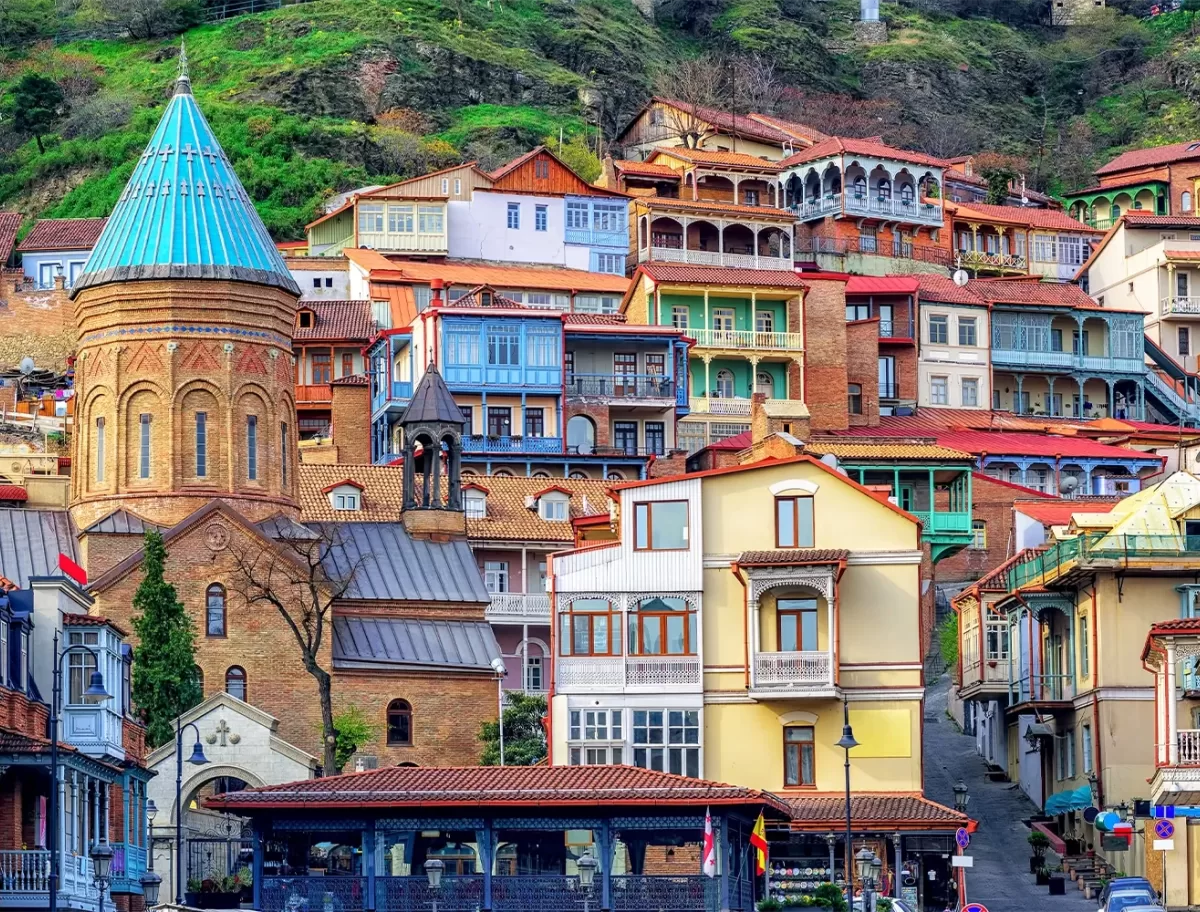 Beautiful landscape photograph of buildings on a hill side in different colours including blue, rusted red and yellow in Tbilisi