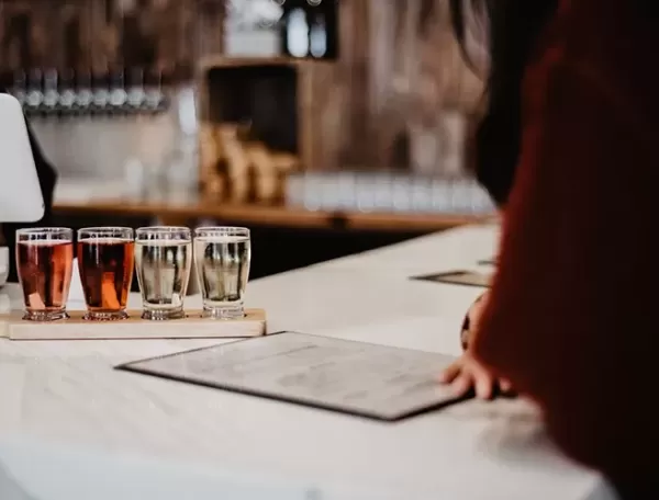 Cider tasting at a table with 8 small glasses of various ciders in wooden holder
