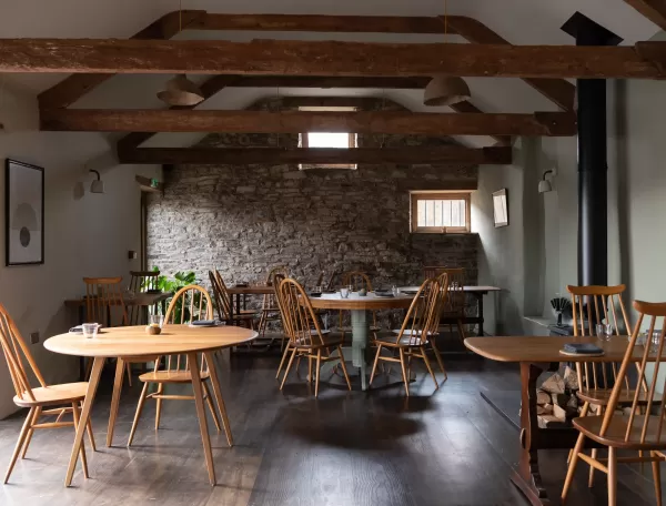 Quint cottage style restaurant interior with Cornish stone walls and round wooden tables under wooden beamed roof at Crocadon Farm, Cornwall