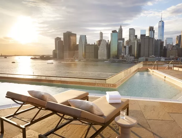 2 lounge chairs set out beside a pool overlooking the New York City skyline.