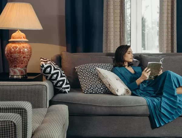 Women in a blue dress lying on the sofa reading a book