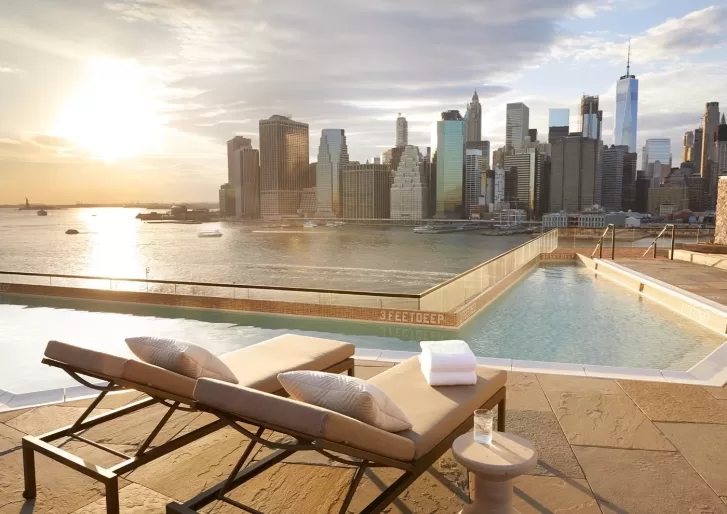 2 lounge chairs set out beside a pool overlooking the New York City skyline.