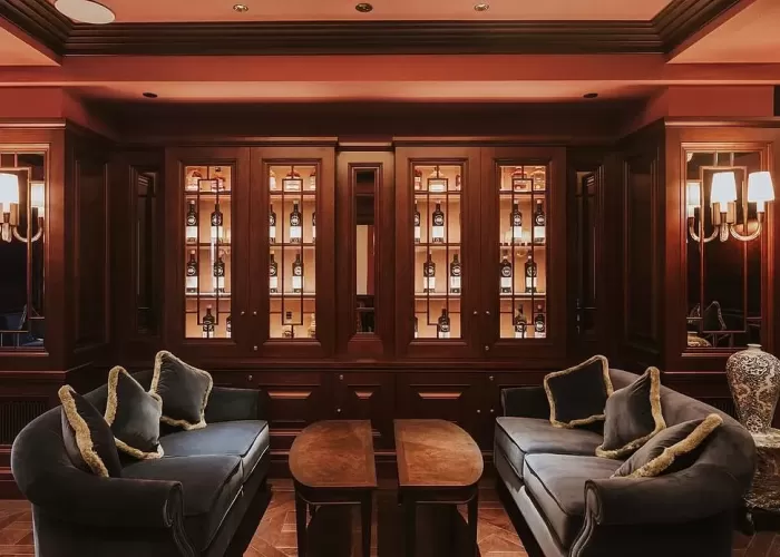 Two blue sofa's with cushions facing each other between two half moon coffee tables in front of wooden wine cabinet