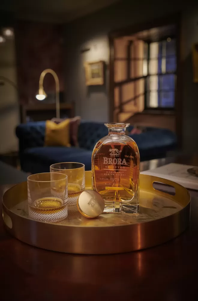 Bottle of Brora whiskey with tasting glasses served on a gold serving plate in a living room with blue sofa at Brora Distillery, Highlands, Scotland