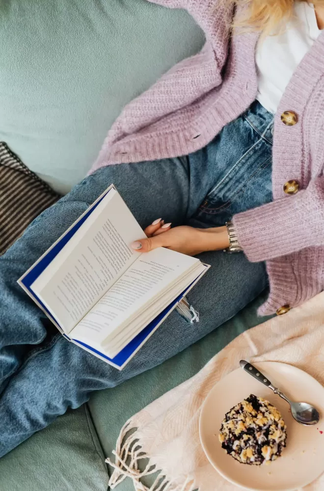 Women in jeans and cardigan reading a book with plate of breakfast
