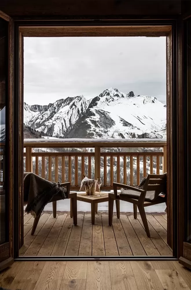 Wooden balcony with low lying chairs and coffee tables with a view on the snowy mountains at M Lodge & Spa, Saint Martin de Belleville