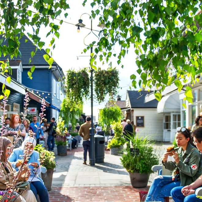 Bicester Village in the sunshine with people sitting and shopping