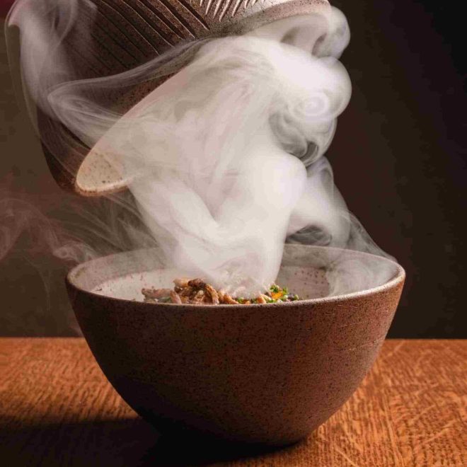 Jollof rice served in wooden bowl with lid and dry ice at Akoko