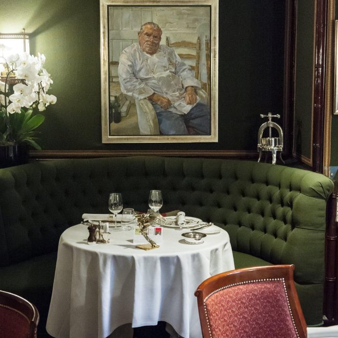 Restaurant dining booth with circular green sofa seating and rounded table in front of a portrait on a green wall