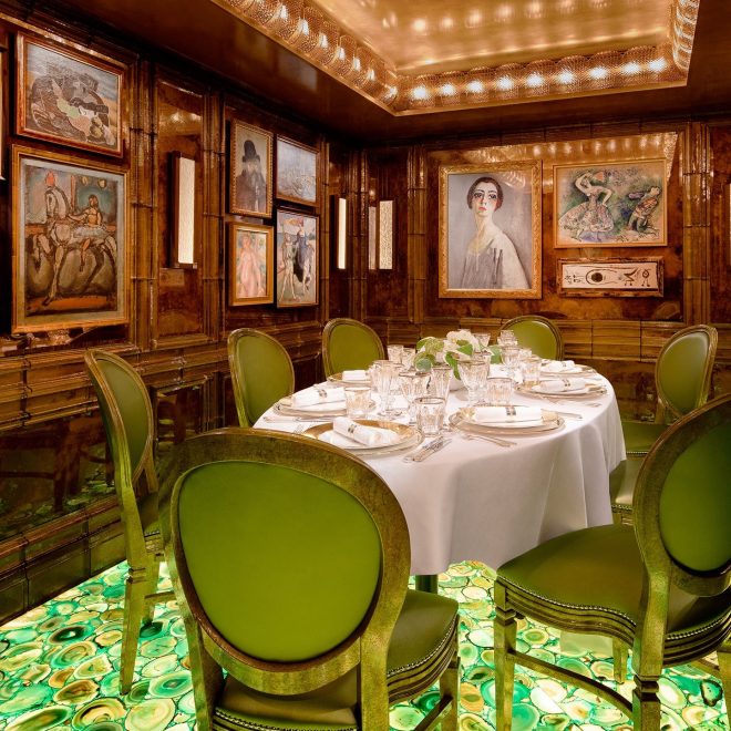 Private round dining table and green luxury dining chairs in wooden room filled with framed paintings on abstract green backlit gemstone floor