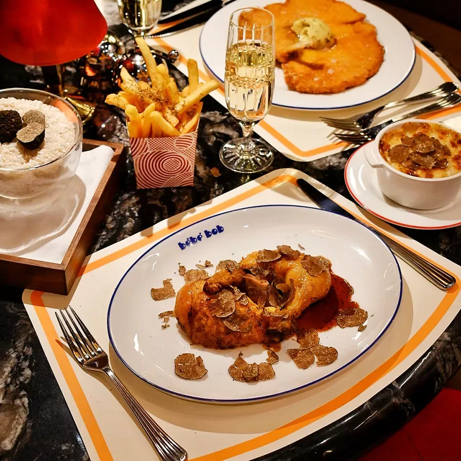 A restaurant table set with roast chicken topped with truffles, a bowl of rice with truffles, a serving of fries, a potato dish, a side dish, and a glass of champagne.