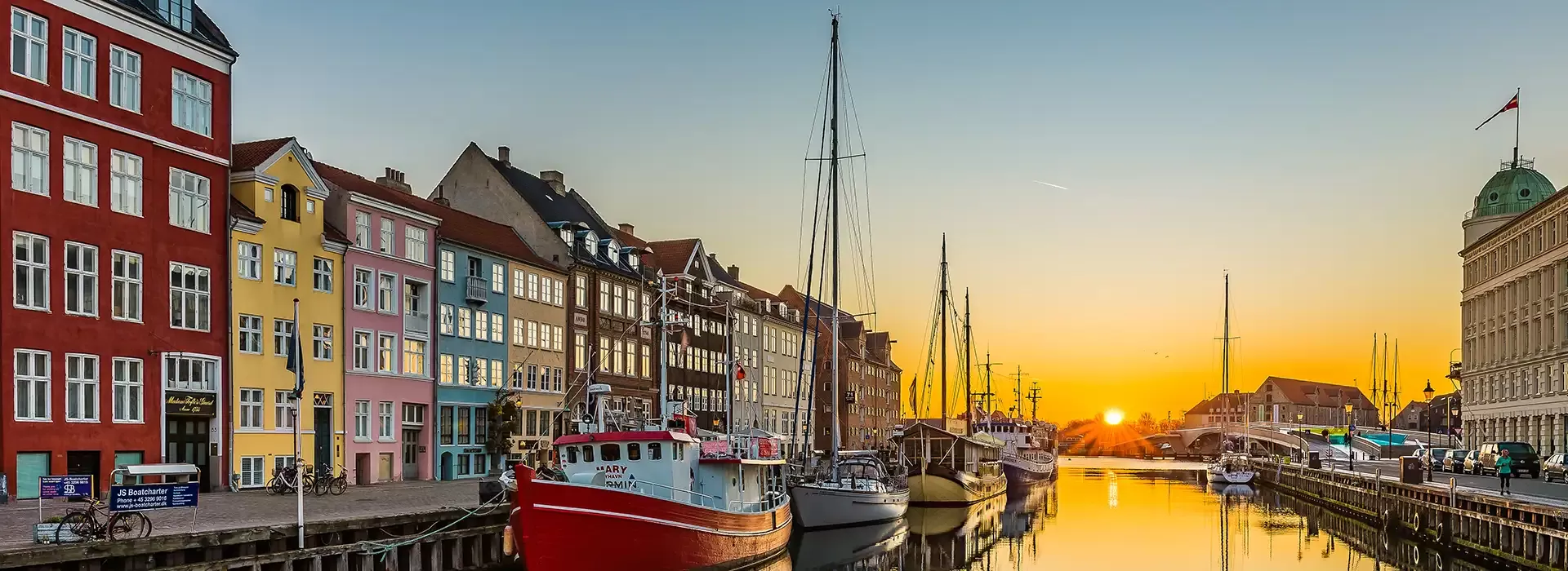 Sunset view of street of colourful houses split between a river with boats