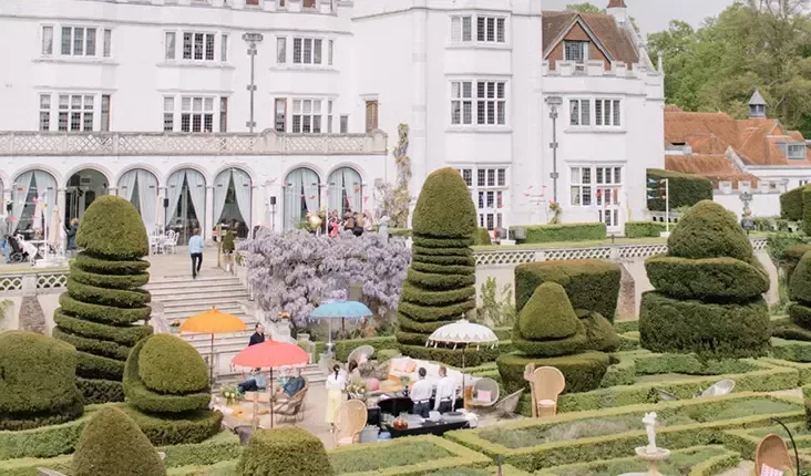 A picturesque garden party is set up on a bright day in front of a large, elegant white building.