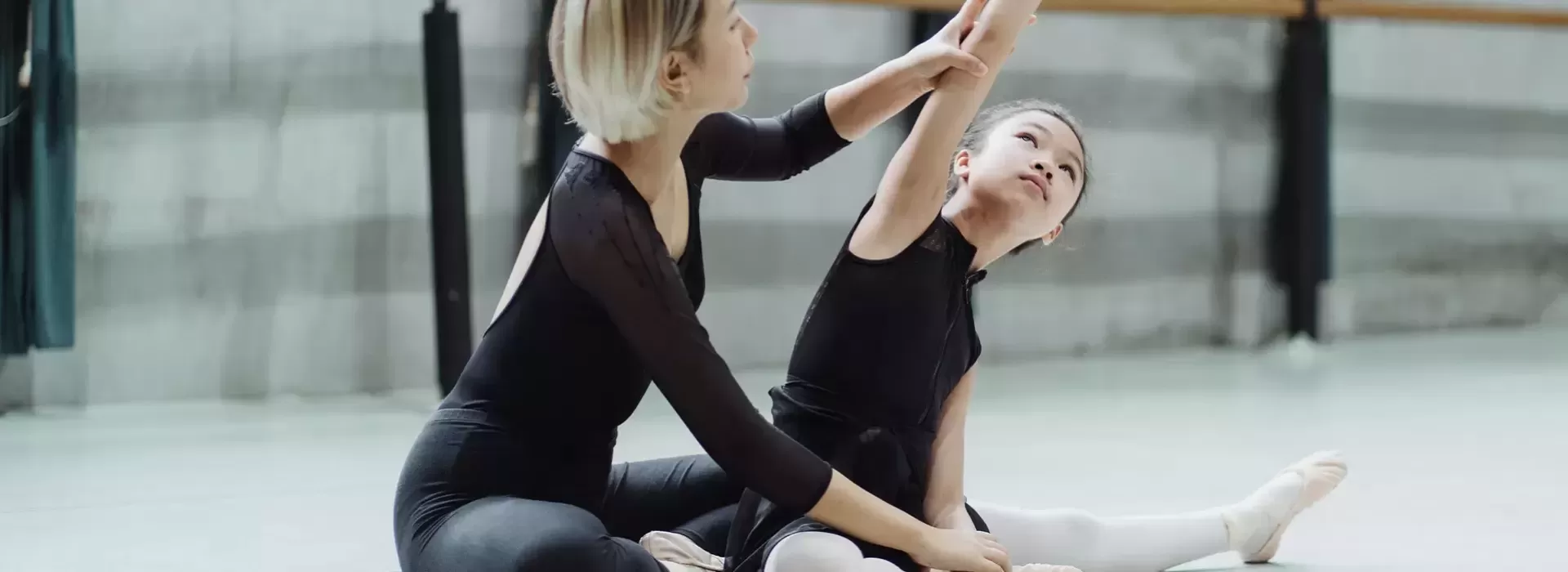 Ballet teacher sat on floor with child student helping her with a pose