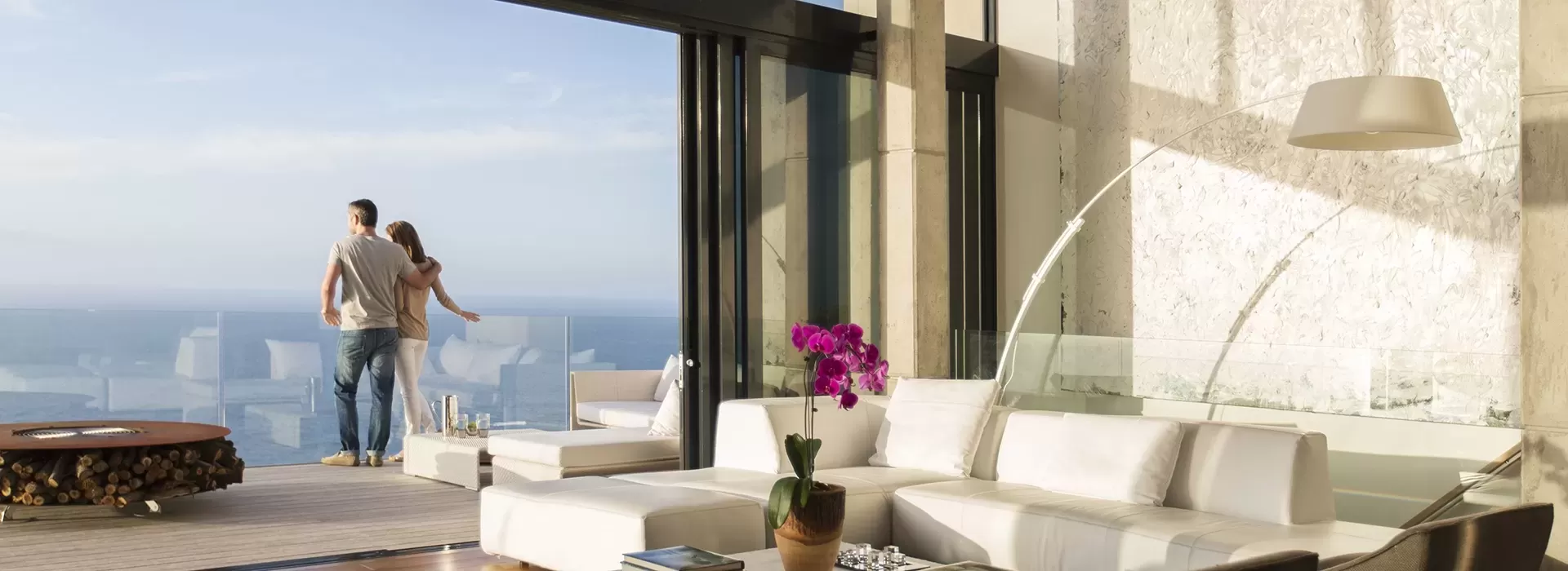 Couple hugging and looking out huge glass window inside luxury penthouse appartment