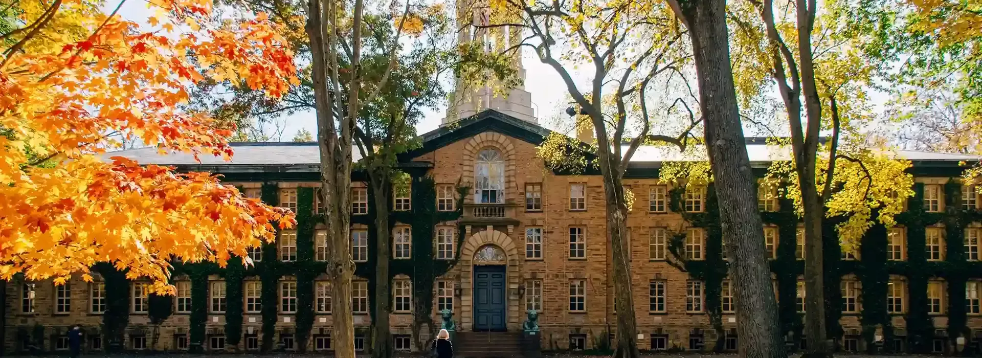 Autumn trees next to large pathway with women walking up to a grand US college