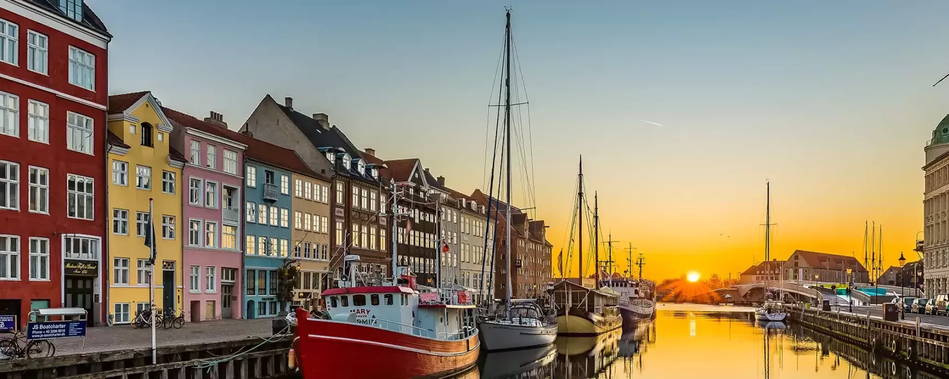 Sunset view of street of colourful houses split between a river with boats