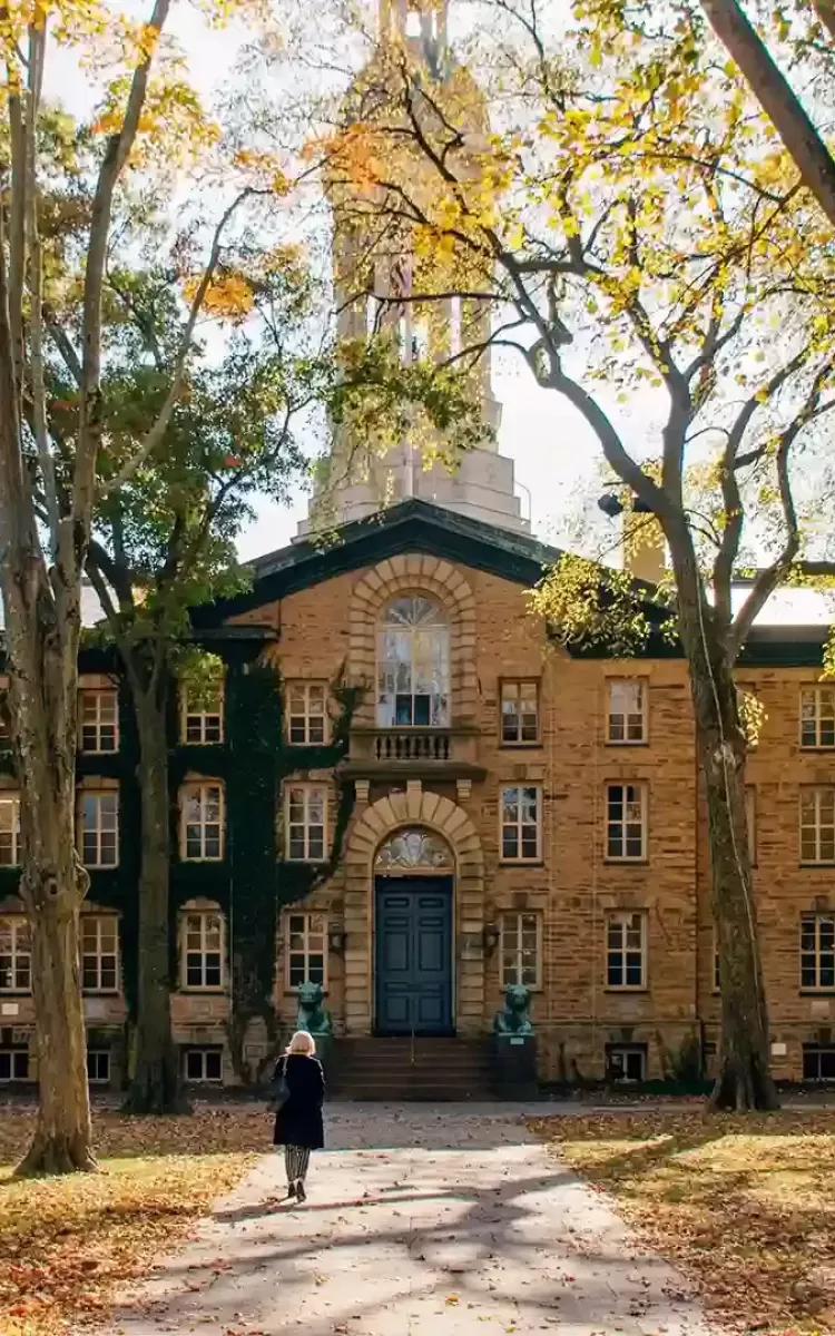 Autumn trees next to large pathway with women walking up to a grand US college