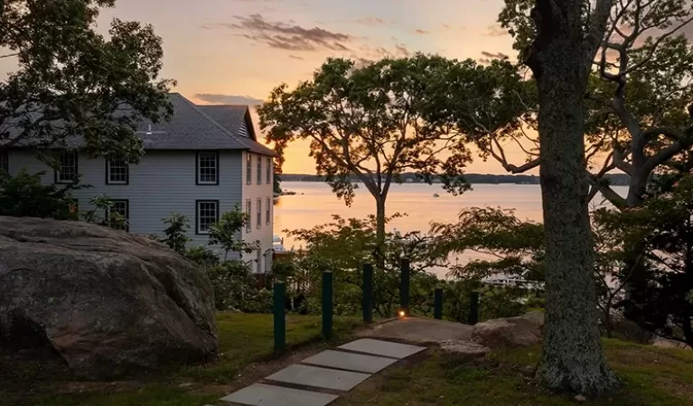 A big house through the treas with a sea few at sunset.