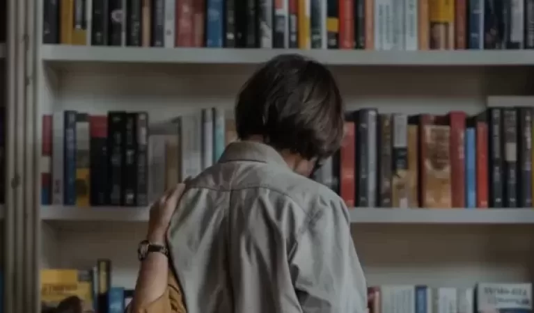 A woman looking at books on a bookshelf, in a library.